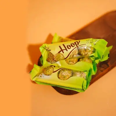 Green-wrapped Hoop candy displayed on a wooden tray with a peach background.