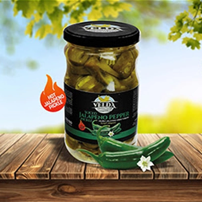 Velda Sliced Jalapeño Pepper Pickle jar displayed on a wooden table with a vibrant outdoor backdrop and a 'Hot Jalapeño Pickle' label.