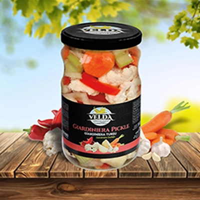 Velda Giardiniera Pickle jar placed on a wooden table with fresh vegetables and a sunny outdoor background.