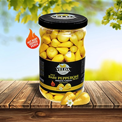 Velda Hot Baby Pepperoni Pickle jar displayed on a wooden table with a vibrant outdoor backdrop and a spicy heat label