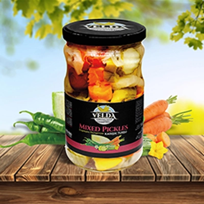 Velda Mixed Pickles jar displayed on a wooden table with fresh vegetables and a sunny outdoor background.