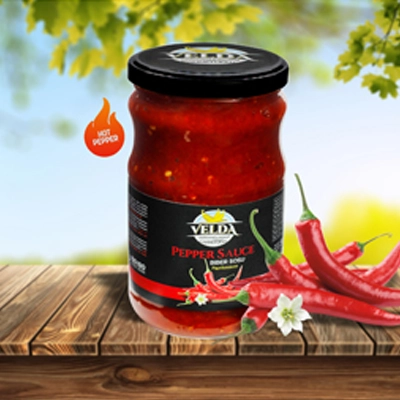 Velda Pepper Sauce jar showcased on a wooden table with fresh red chilies and a vibrant outdoor background.